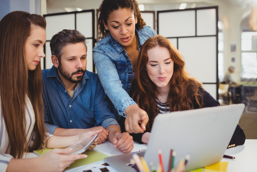 businesswoman pointing at laptop with coworkers at desk in creative office