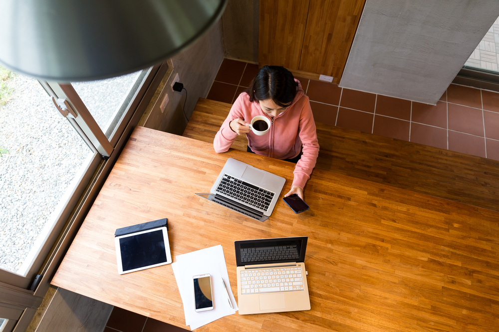 top view of woman drinking coffee while checking laptop and cellphone